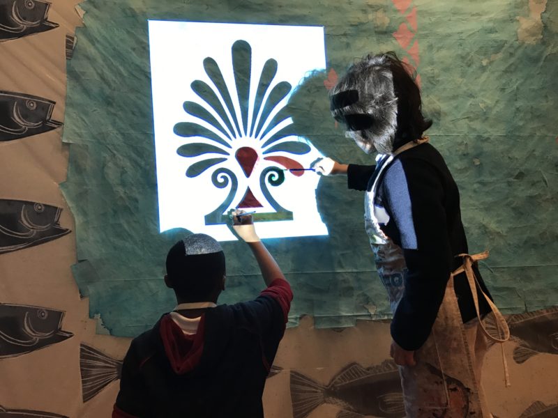 Two kids paint a mural of a floral motif