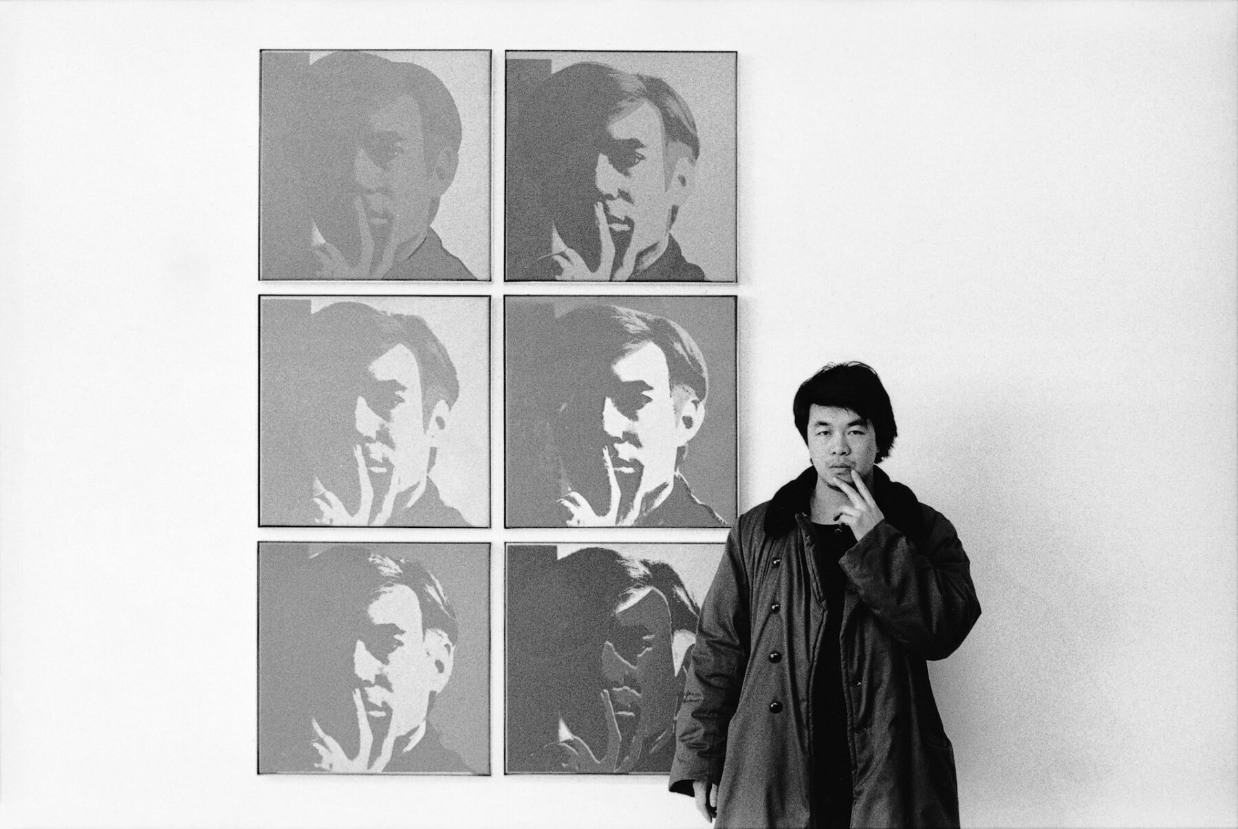 Artist Ai Weiwei stands in front of portraits of Andy Warhol, mimicking his pensive pose