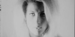 A blonde woman with voluminous hair and heavy eye makeup gazes directly into the camera in this black-and-white film still. The image is blurry and full of light, giving the image a dreamlike quality.