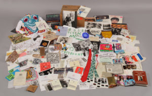 The contents of one of Warhol’s Time Capsules. There are several books, pieces of artwork by Keith Haring and Jean-Michel Basquiat, a hand painted turtleneck by Kenny Scharf with a large, blue cartoonish face painted on the front, a Mickey Mouse figurine, ties, postcards, and documents, among other things.