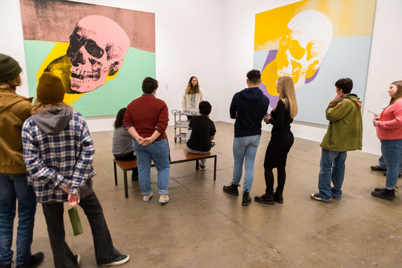 1. A Youth Arts Council teen giving a gallery talk to a group on museum goers in front of Warhol’s large skull paintings during the Winter Teen Night event.