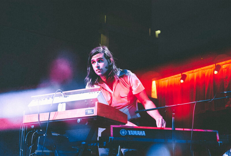 A person playing a Yamaha keyboard onstage under blue and pink stage lighting.