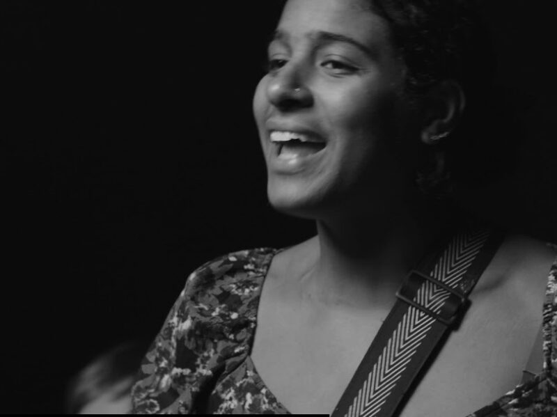 Screen grab from live performance, in black and silver. Leyla McCalla sings.