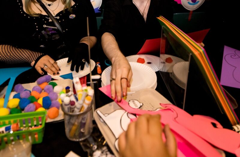 A group of people engaging in arts and crafts, using colorful materials like markers, paper, and pompoms on a table.