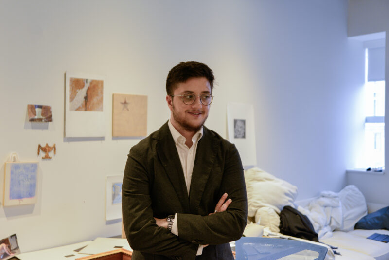 A head shot of Max Tristan Watkins posing in front of his artwork